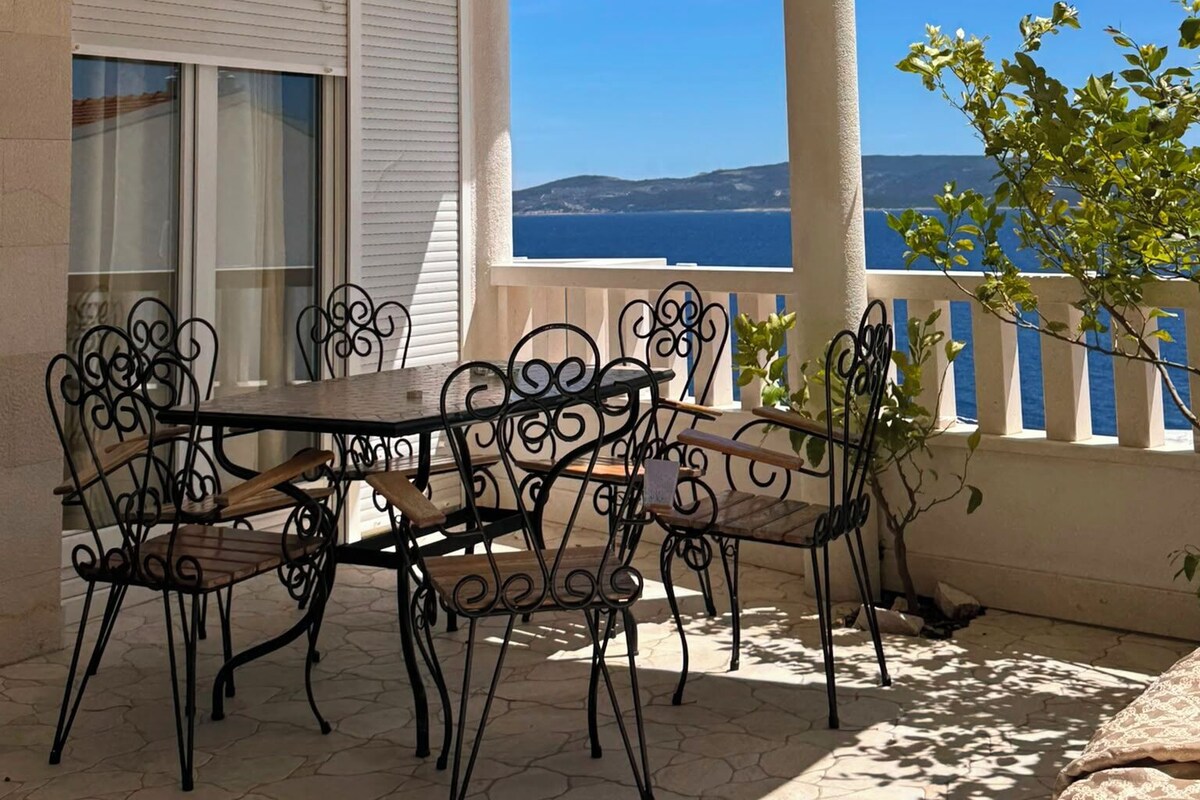 An outdoor patio with a table and chairs, a white awning, and a view of the sea.