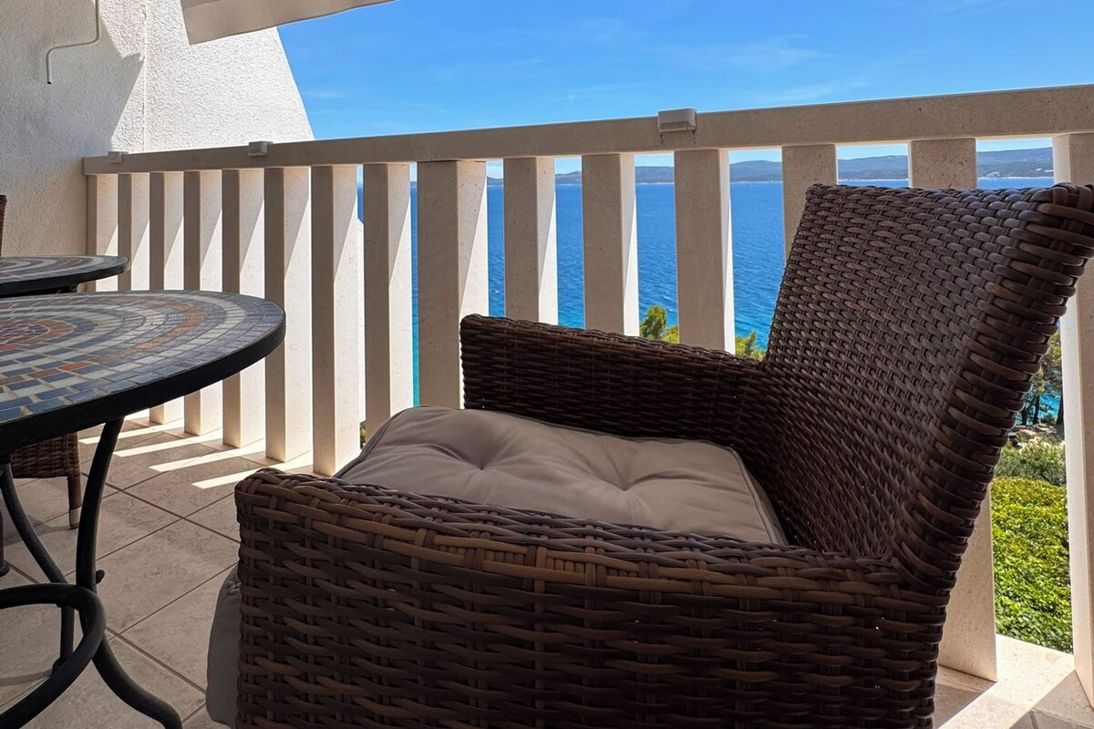 A wicker chair with a cushion on a balcony with a view of the sea.
