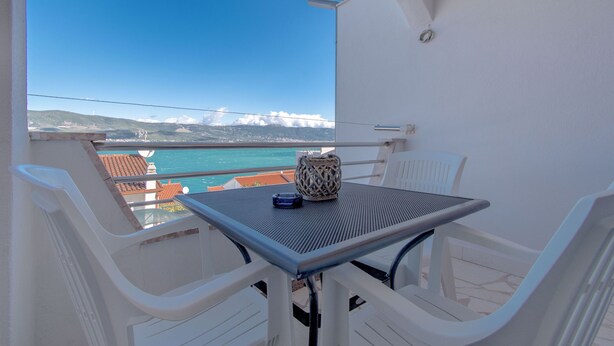 Ein Balkon mit Tisch und Stühlen, der Blick ins Küstenland mit Gebäuden und Bergen in der Ferne bietet.