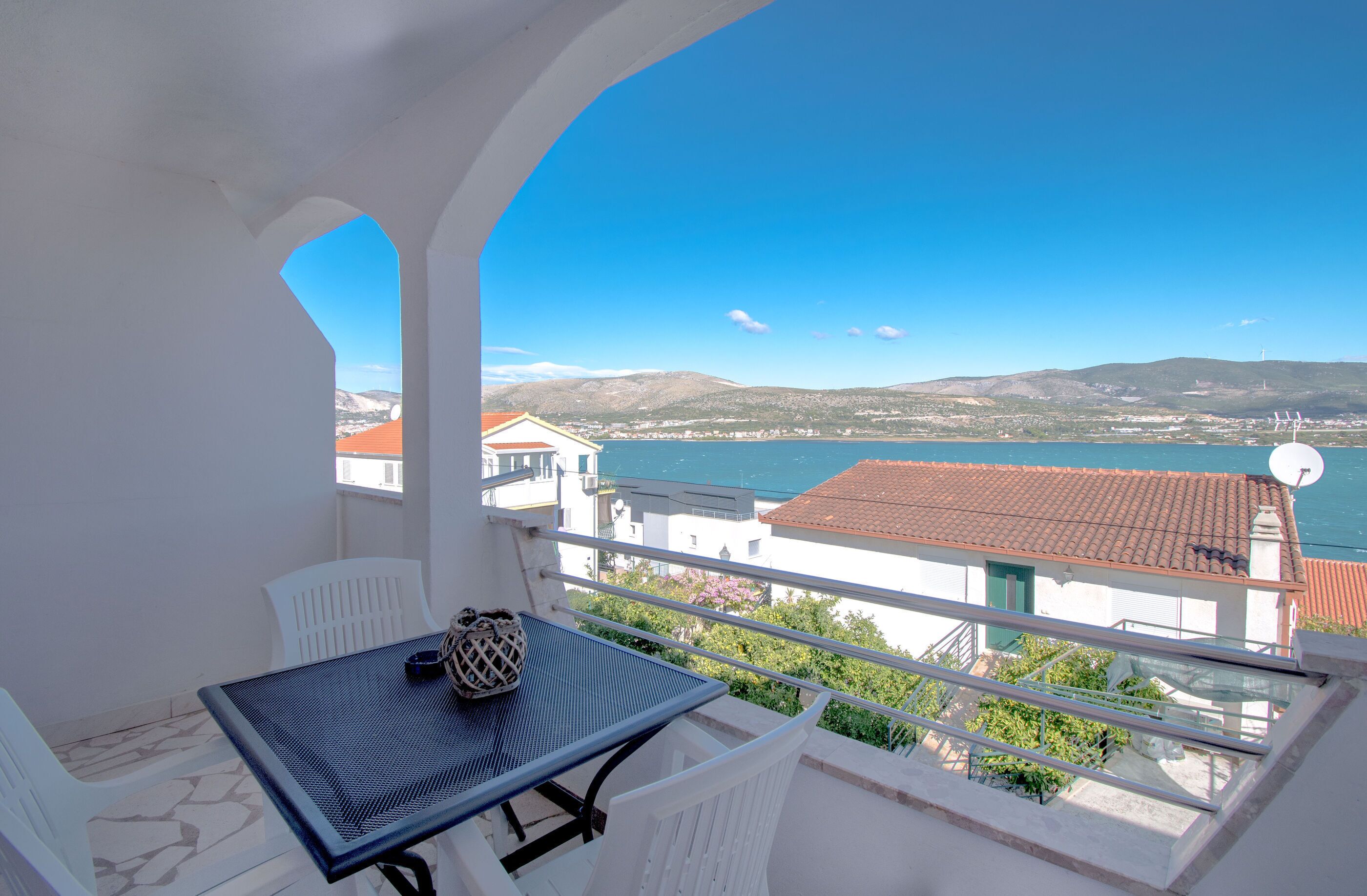 A balcony with a table and chairs, overlooking a coastal town and sea.