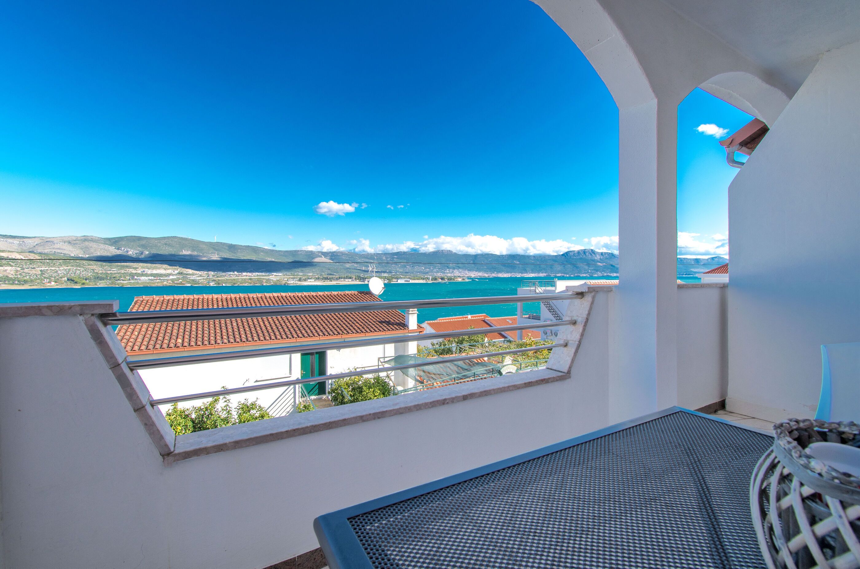 A balcony with a clear view of a coastal landscape, including a body of water and distant mountains.