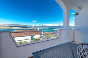A balcony with a clear view of a coastal landscape, including a body of water and distant mountains. - Apartments Iva (Arbanija)