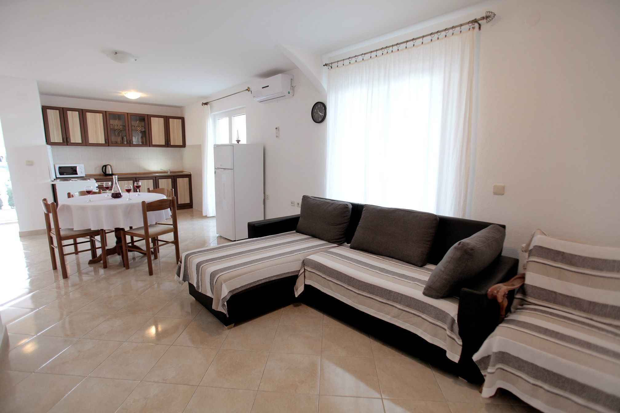 A living room with a sofa, a dining table with chairs, a kitchen area, and a window with curtains.