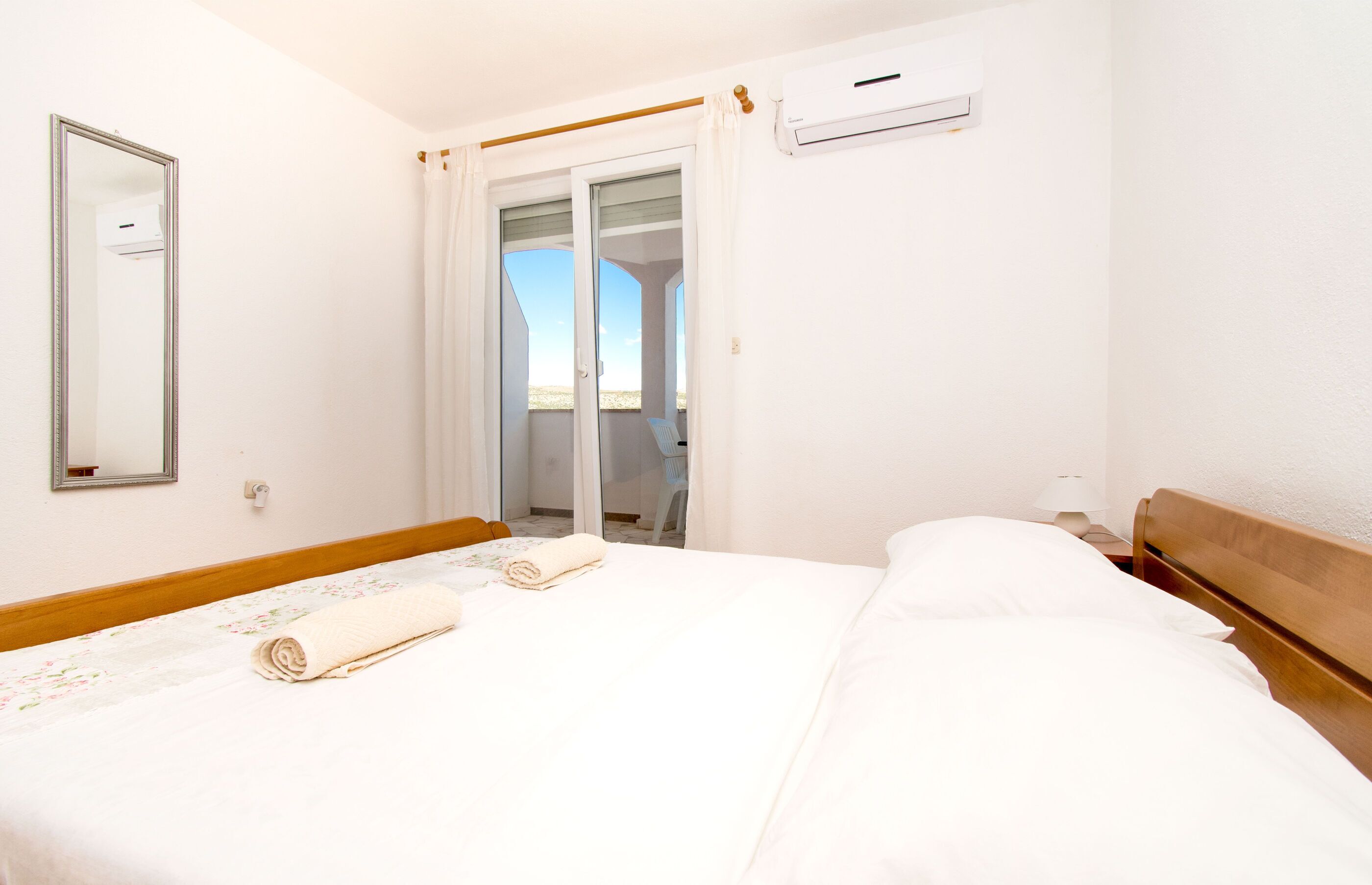 Ein Hotelzimmer mit Bett, Spiegel, Klimaanlage und Blick durch eine Glastür.