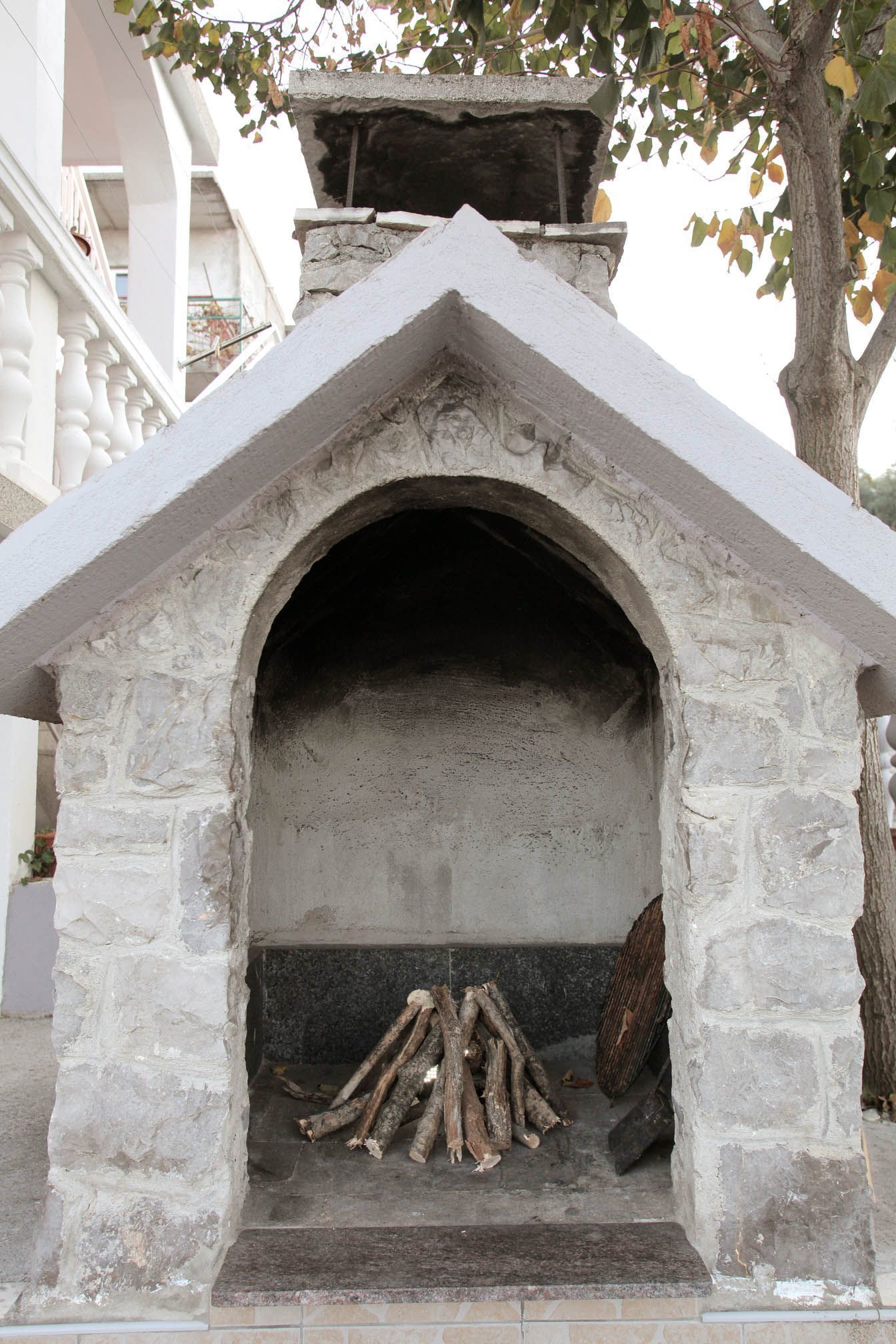 Chimenea de piedra con un diseño de arco sencillo, rodeada por una barandilla blanca y un árbol.