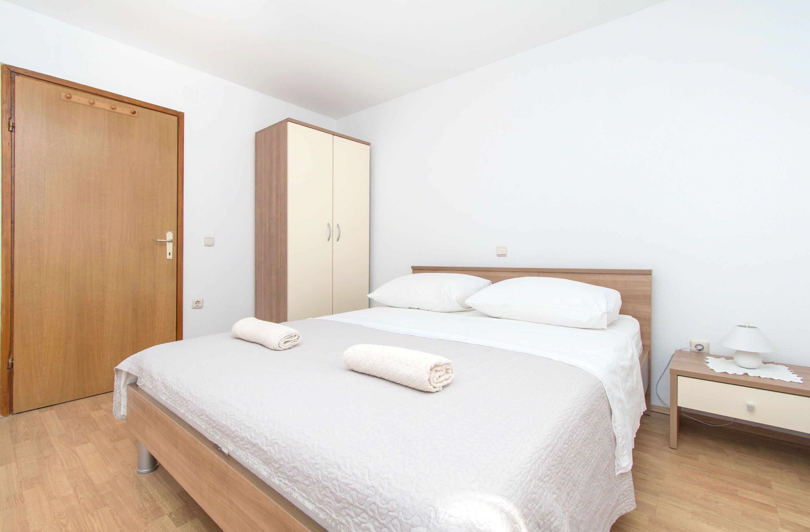 Une chambre à coucher avec une armoire en bois, un lit avec du linge de lit blanc et une table de chevet avec une lampe.