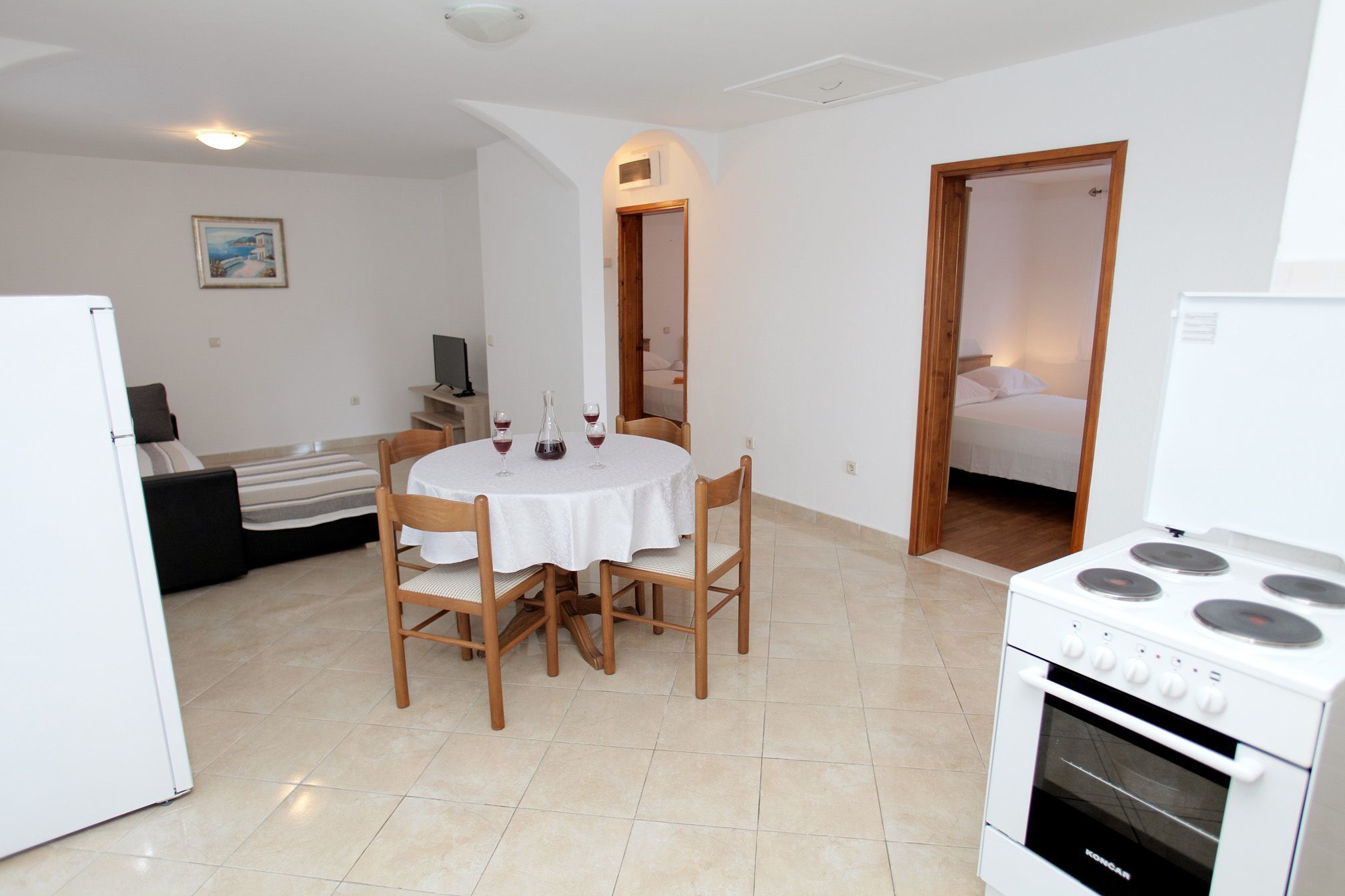 A compact kitchen with a white stove, a dining table with four chairs, and a small seating area with a sofa and a TV.