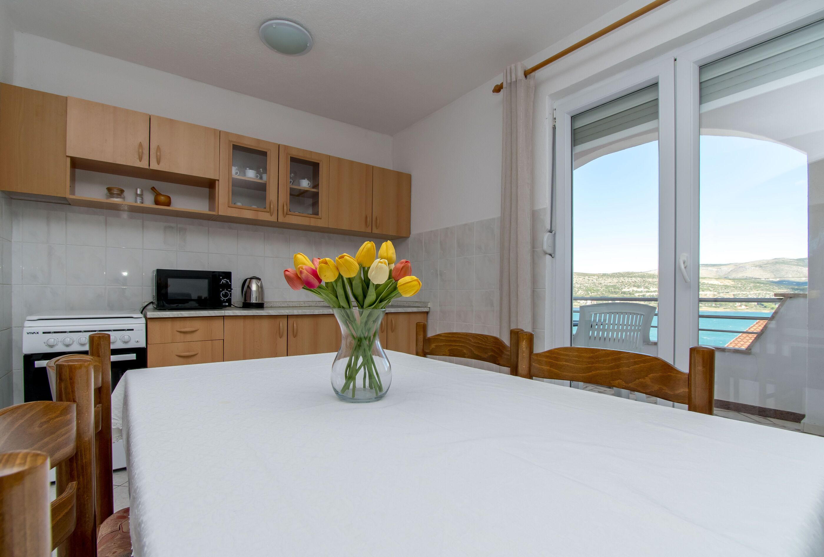 Une cuisine moderne avec des meubles en bois, un four à micro-ondes et une cuisinière. On y trouve une table à manger ornée d'un vase de fleurs au centre.