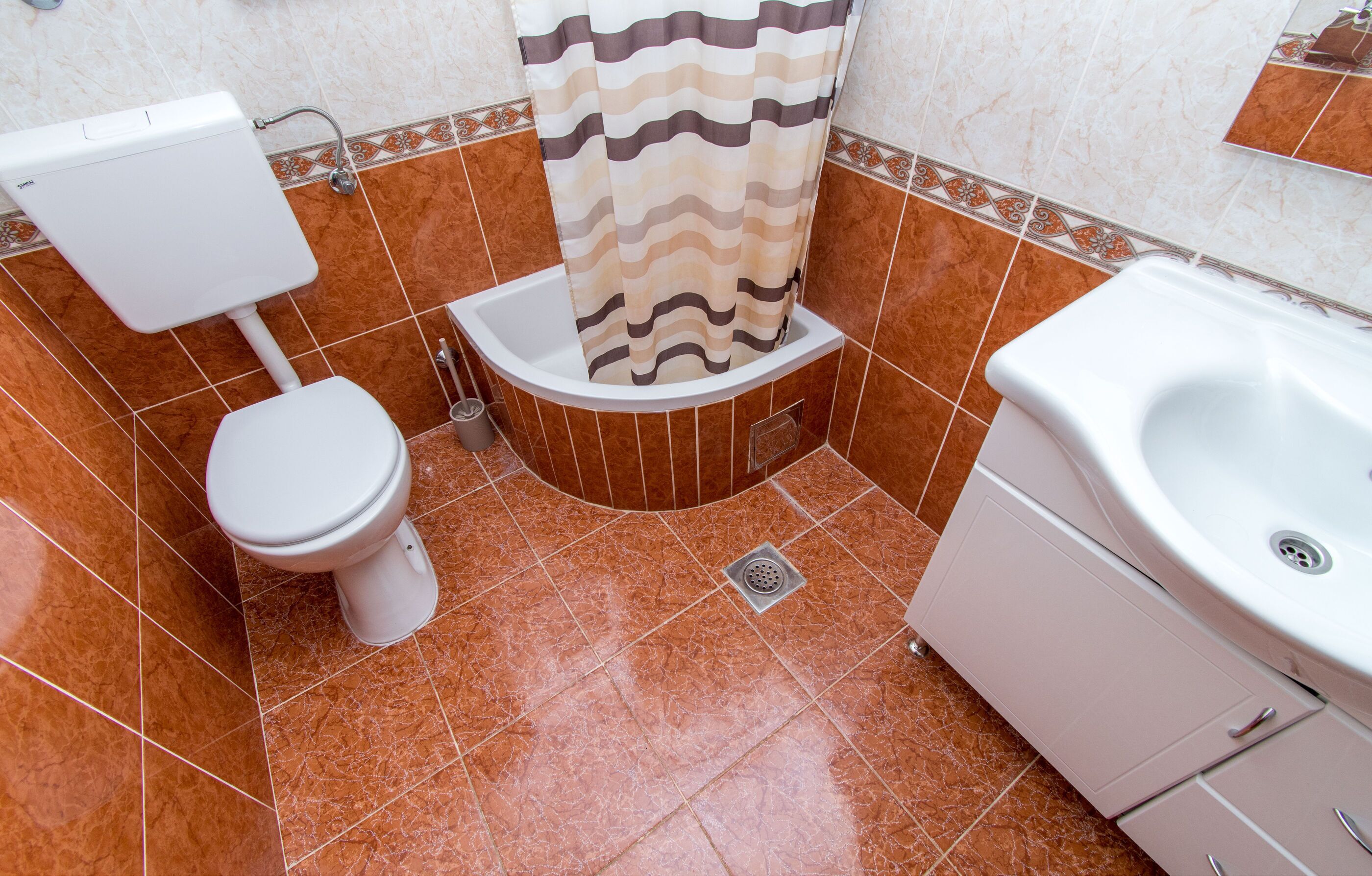 A bathroom with a toilet, a shower with a patterned curtain, and a sink.