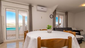 Ein Zimmer mit rundem Tisch, Stühlen, einem Blumentopf, einer Couch und Meerblick durch große Schiebetüren.