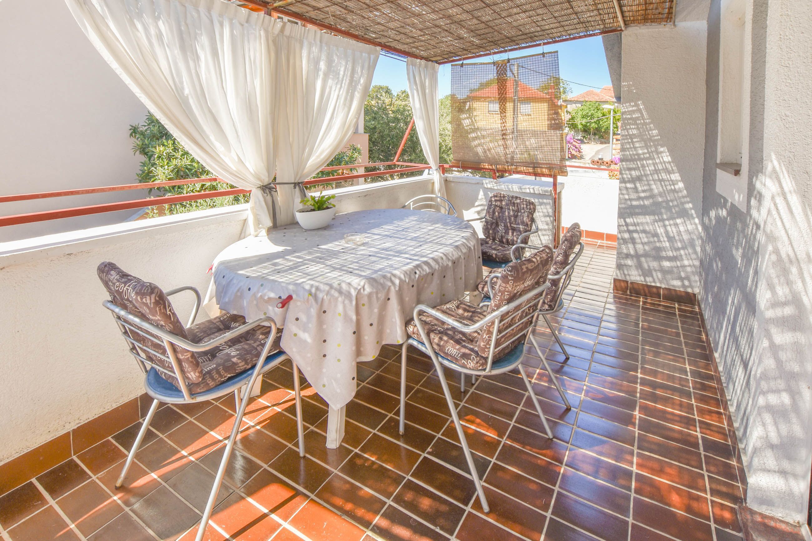 A balcony with a table and chairs, a potted plant, and a view of the neighborhood.