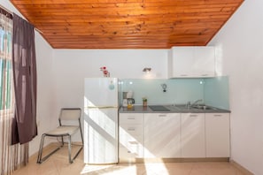 A compact kitchen with white cabinets, a stainless steel sink, and a wooden ceiling. - Apartments Anita (Srima)