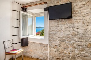 Una stanza con una parete in pietra, una finestra vista mare, una TV a parete e una poltrona con cuscino.