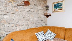 A room with a stone wall, a framed painting, and a brown sofa with patterned cushions. - Apartments Islandbreeze (Prvic Sepurine)