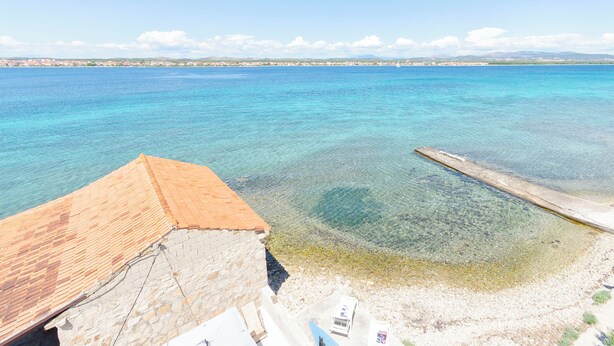 A coastal view with a clear blue sea, a wooden pier, and a building with a tiled roof. - Apartments Islandbreeze (Prvic Sepurine)