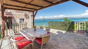 A covered outdoor seating area with a table and chairs, overlooking a body of water. - Apartments Islandbreeze (Prvic Sepurine)