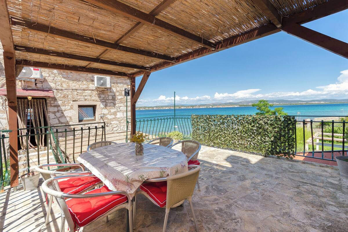 A covered outdoor seating area with a table and chairs, overlooking a body of water.