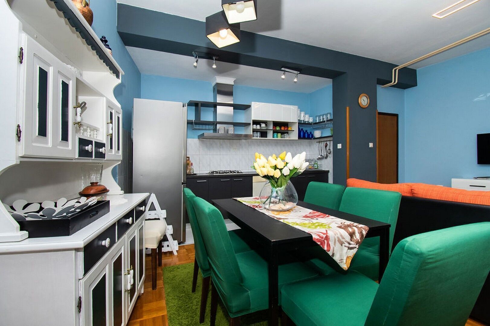 A compact kitchen with white cabinets, a refrigerator, and a dining area with green chairs and a table.