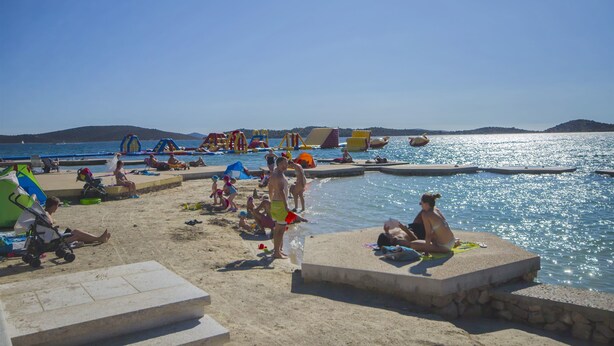 En strand med solstolar, parasoller och en swimmingpool.