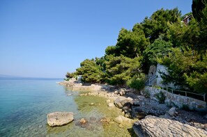 Zona costera con aguas cristalinas, costa rocosa y vegetación densa.