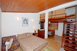 A bedroom with a bed, a sofa, a fan, a lamp, and a staircase leading to a kitchen area. - Apartments Aida (Omis)
