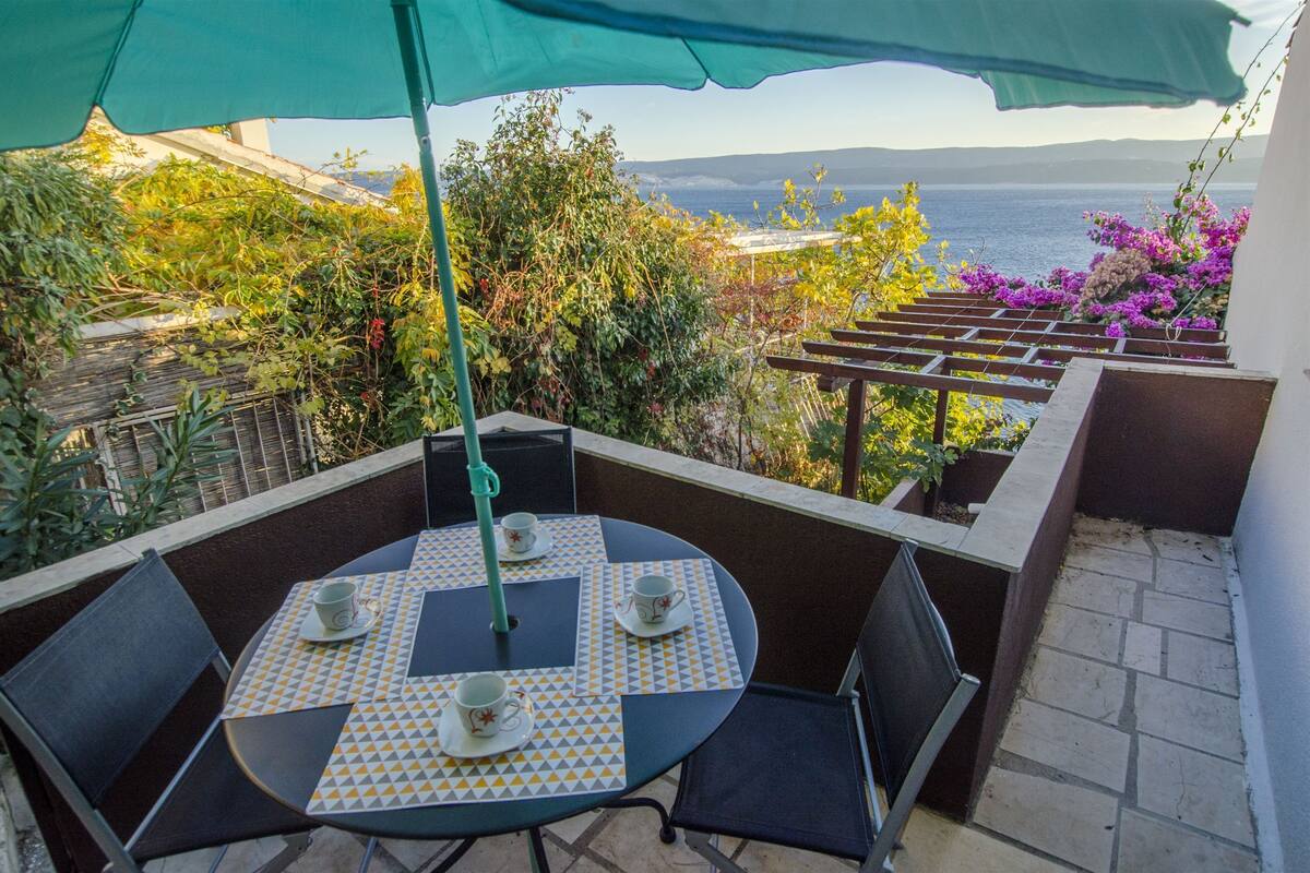 A patio with a table set for two, chairs, and an umbrella.