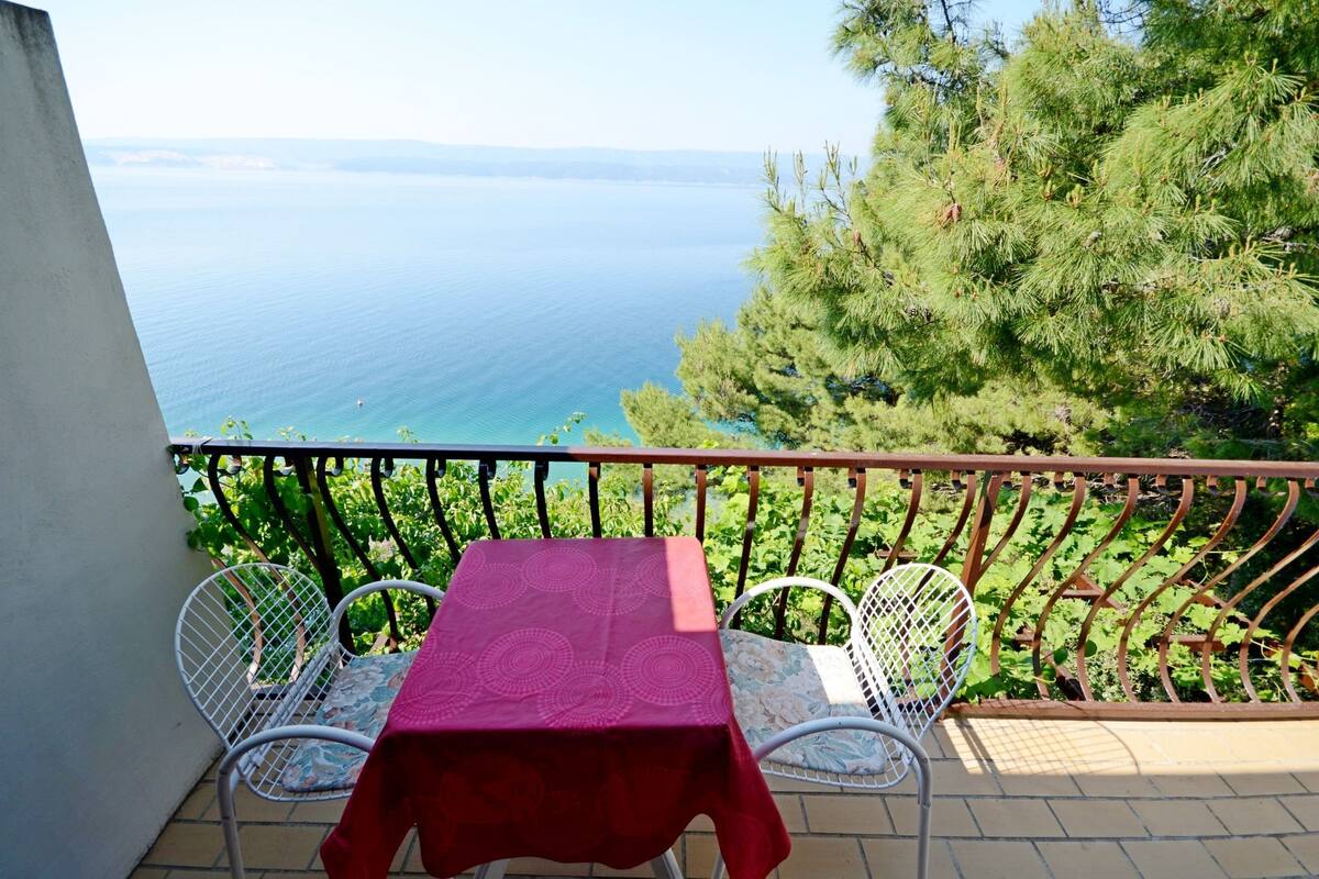 A balcony with a table and chairs, overlooking a body of water and greenery.