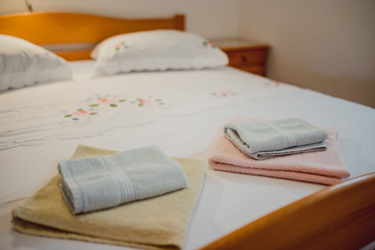 Una cama bien tendida con una colcha de estampado floral, dos toallas dobladas y un cabecero de madera.