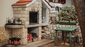 A stone-built outdoor kitchen with a tiled roof, a table, and chairs. - Apartments Antun (Ivan Dolac)