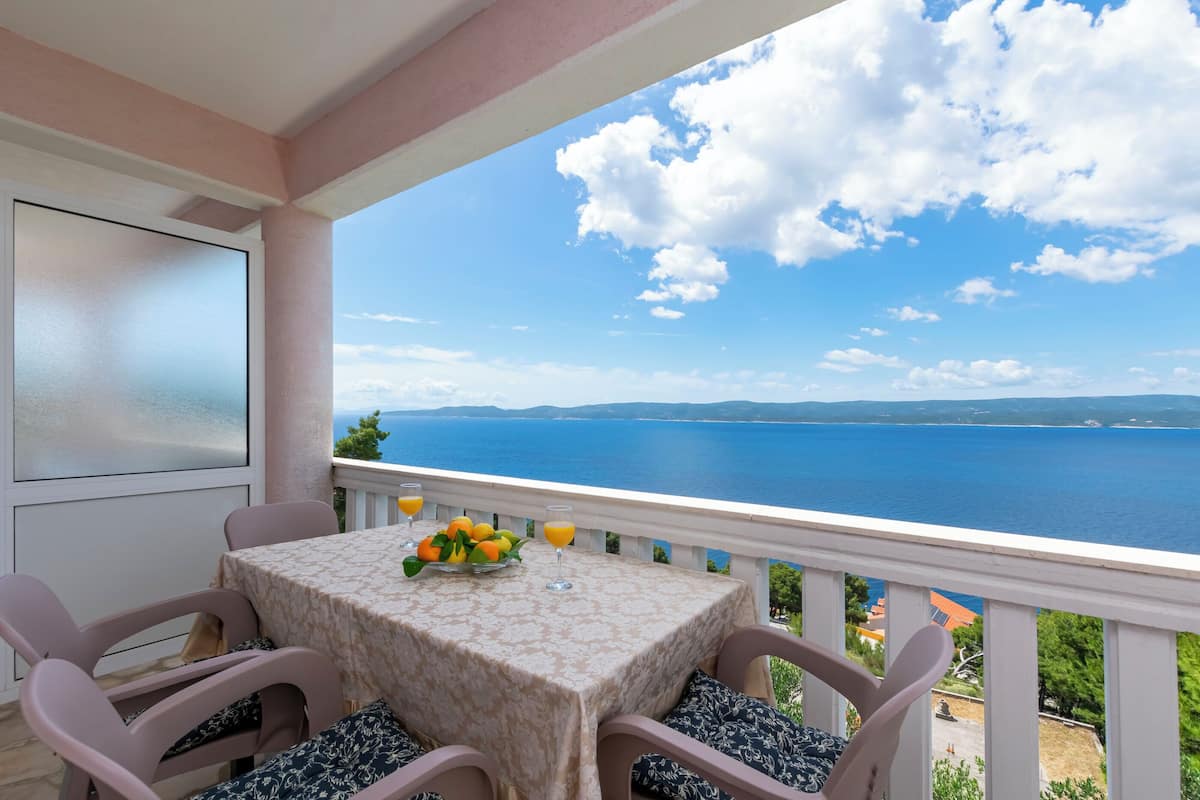 A balcony with a table set for two, overlooking a scenic view of the sea and distant land.