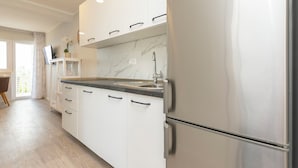 Una cocina moderna con armarios blancos, salpicadero de mármol, refrigerador de acero inoxidable y pileta integrada.