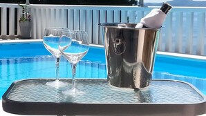 Mesa junto a la piscina con un balde de metal que contiene una botella y vasos.