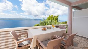 Un balcón con una mesa dispuesta para dos, con vistas a un paisaje marino y tierra a lo lejos.