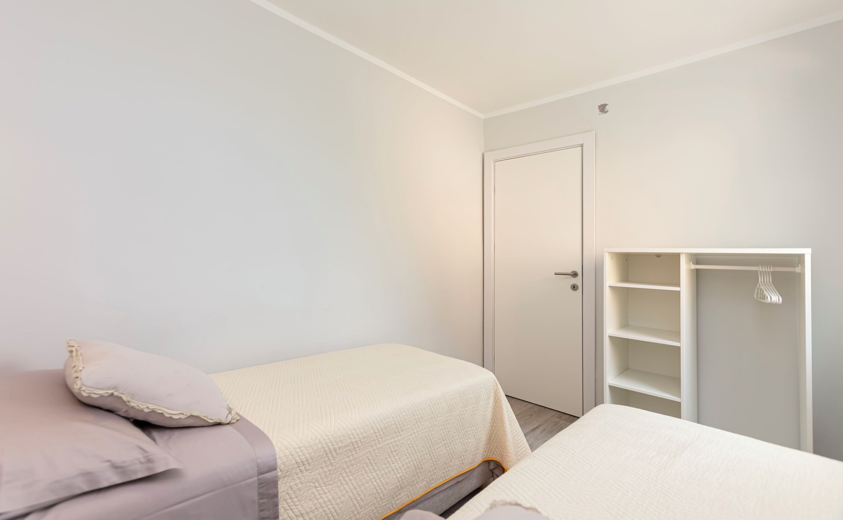 A small, clean room with two beds, a wardrobe, and a door.