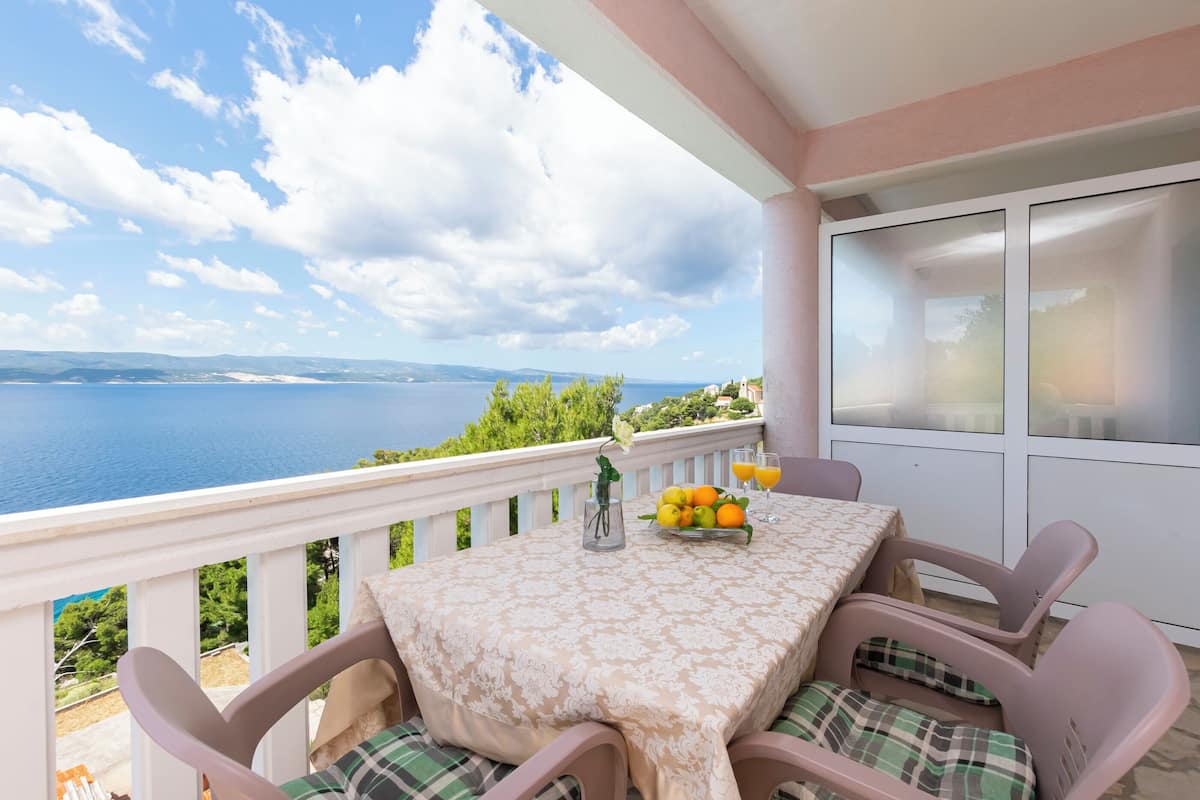 A balcony with a table set for two, overlooking a body of water and greenery.