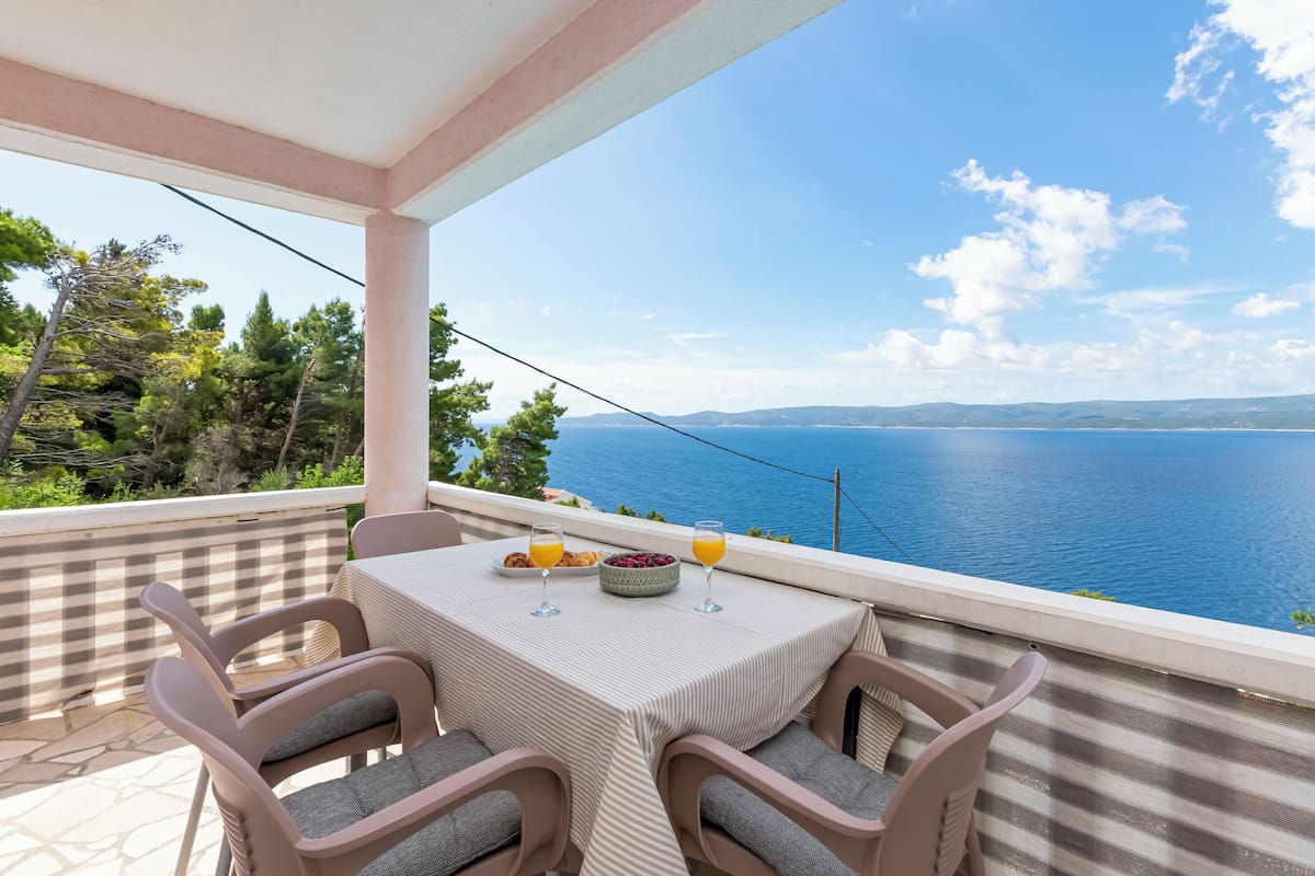 A balcony with a table set for two, overlooking a sea view.