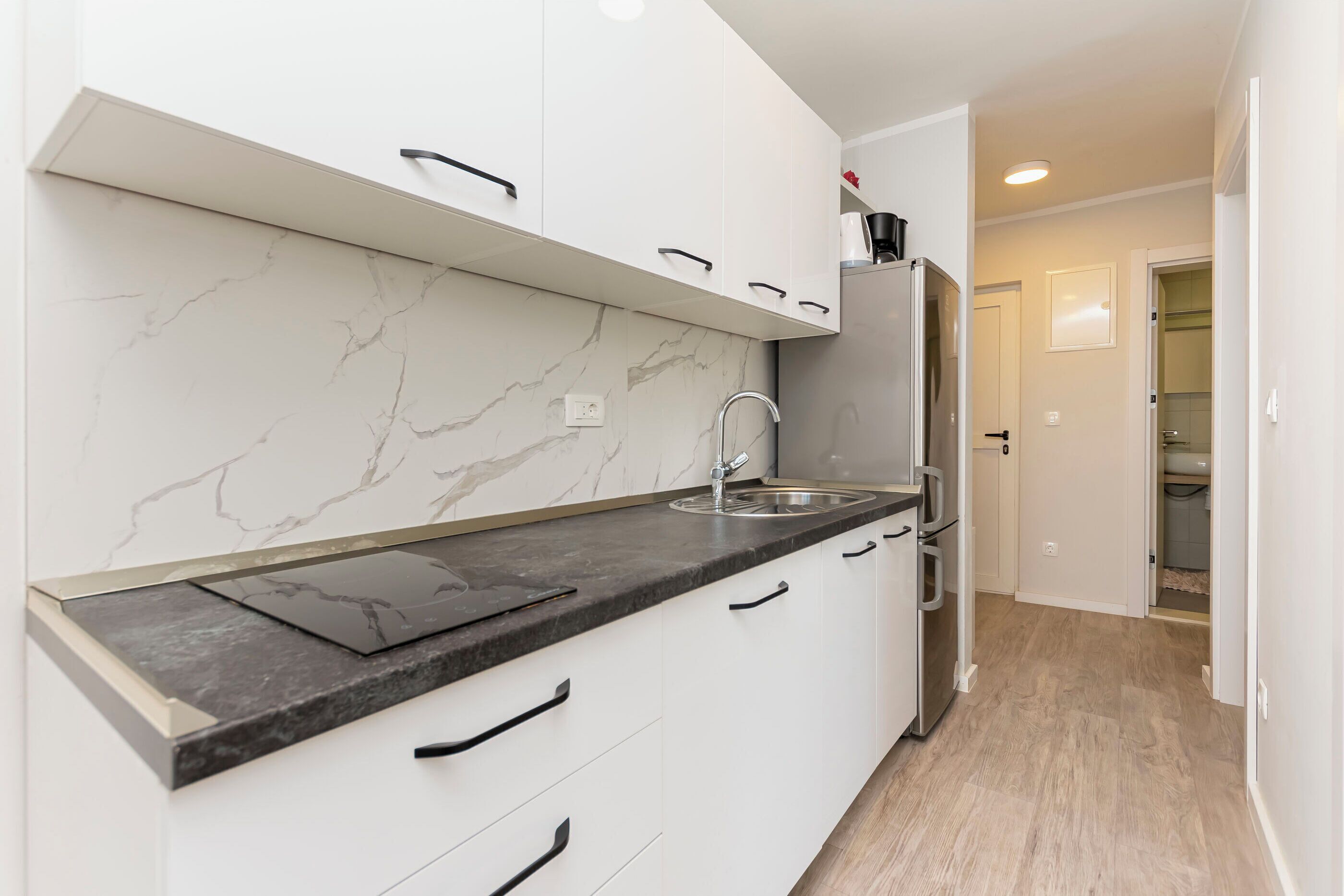 A modern kitchen with white cabinets, a marble backsplash, and a black countertop.