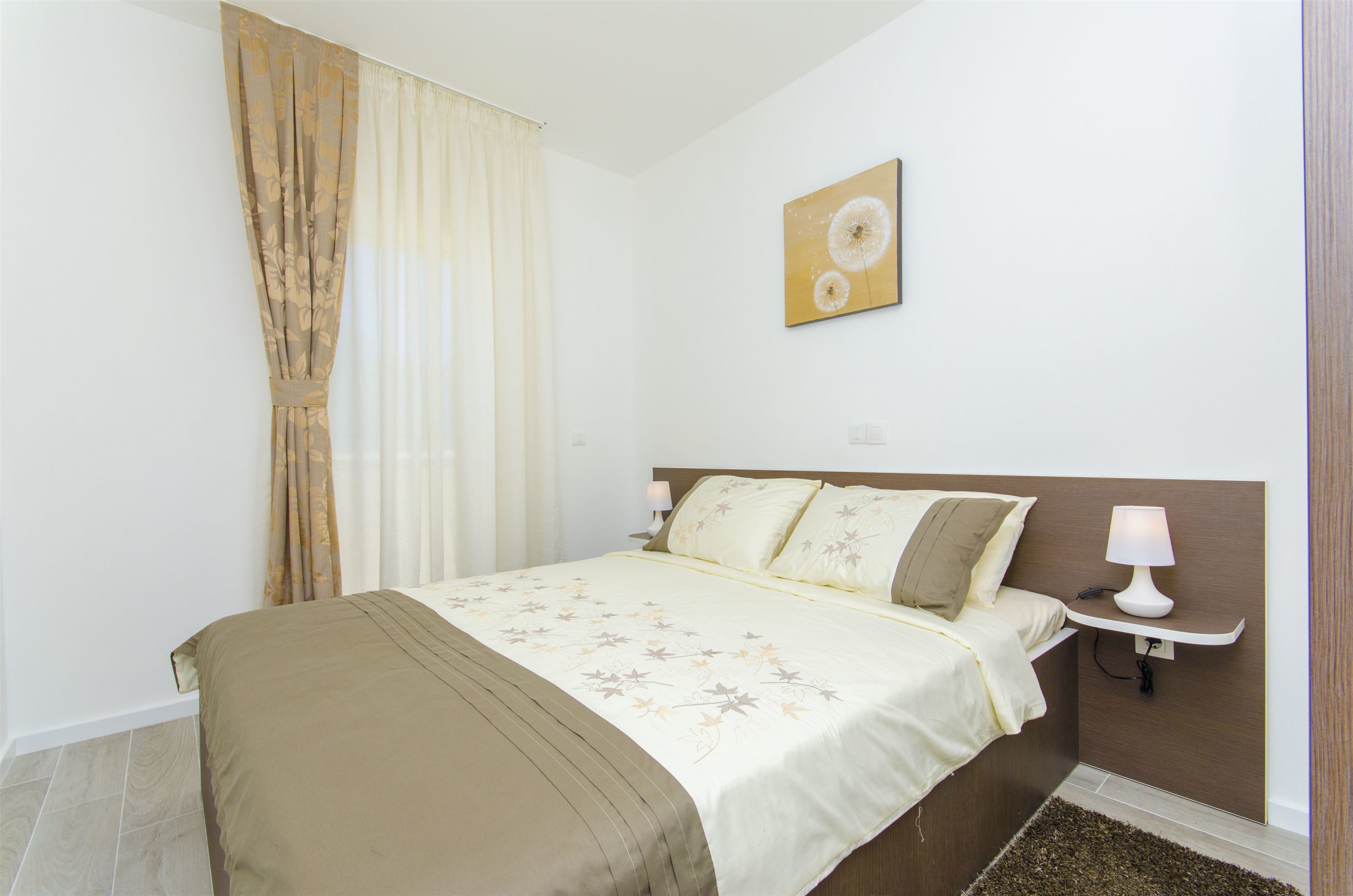 A bedroom with a bed, a nightstand, a wall-mounted lamp, and a painting.