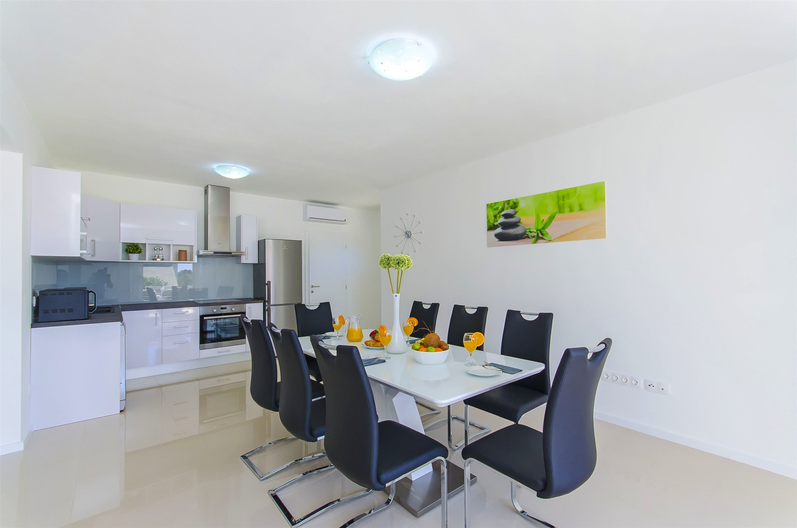 A modern kitchen with white cabinets, a built-in oven, and a dining area with a white table and black chairs.
