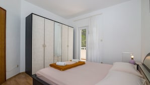 Ein Schlafzimmer mit einem Bett, einem Kleiderschrank, einem Nachttisch mit Lampe und einem Fenster mit Vorhängen.