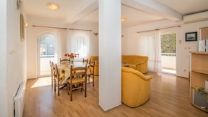 Ein geräumiges Wohnzimmer mit Esstisch, gelber Couch und einem Balkon mit Blick.