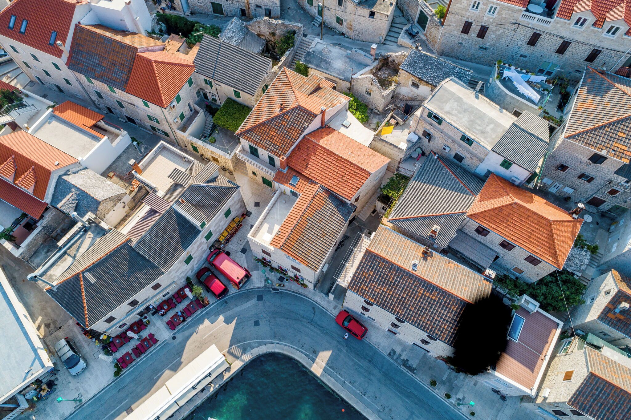 Vista aérea de un pueblo costero con edificios de tejados de terracota, calles estrechas y un muelle visible.