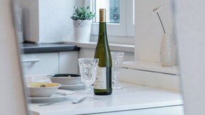 Une table de salle à manger blanche, avec une bouteille de vin, des verres et une petite plante en pot.
