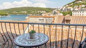 Un balcon avec une table et une chaise, donnant sur une zone côtière avec des bâtiments et de la végétation.