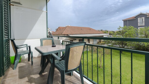 Ein Balkon mit Tisch und Stühlen, einem grünen Geländer und Blick auf benachbarte Häuser und einen Baum.