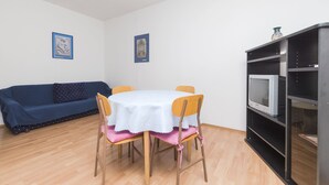 Ein Essbereich mit einem runden Tisch, Stühlen, einem blauen Sofa und einem Fernseher auf einem Regal.