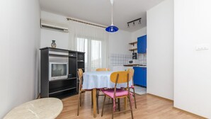 Eine kompakte Küche mit Essbereich, inklusive Tisch mit Stühlen, kleinem Backofen und einer blauen Pendelleuchte.