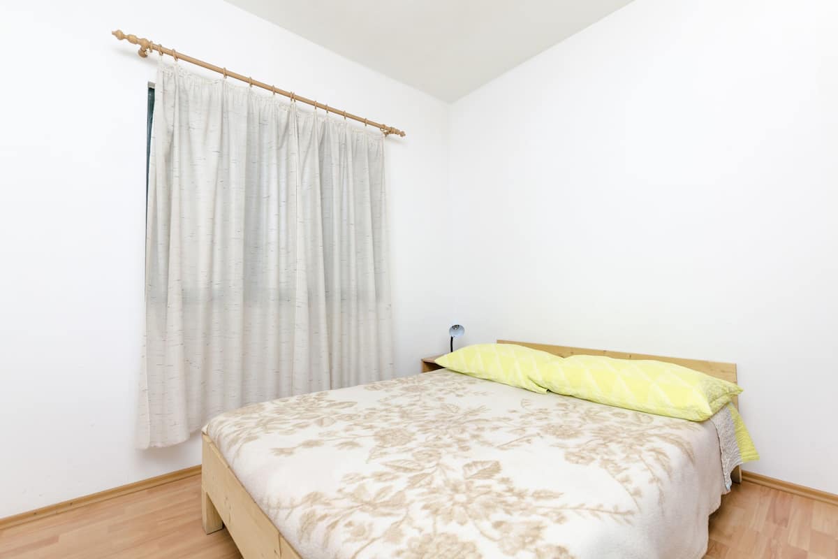 A bedroom with a bed, a wooden headboard, a nightstand, a lamp, and a window with a curtain.