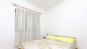 Ein Schlafzimmer mit einem Bett, einem hölzernen Kopfteil, einem Nachttisch, einer Lampe und einem Fenster mit Vorhang.