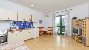 Eine kompakte Küche mit Mikrowelle, Herd und Schränken, ein Essbereich mit Tisch und Stühlen sowie ein Fernseher auf einem Holzboden.